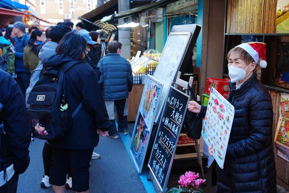 12月18日，在日本东京筑地站附近，餐厅店员在路旁招揽生意。新华社记者贾浩成摄