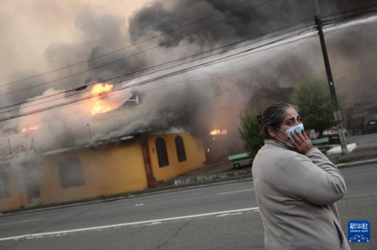 1月18日,在智利比奥比奥大区彭科市,一名女子站在燃烧的建筑前。新华社发